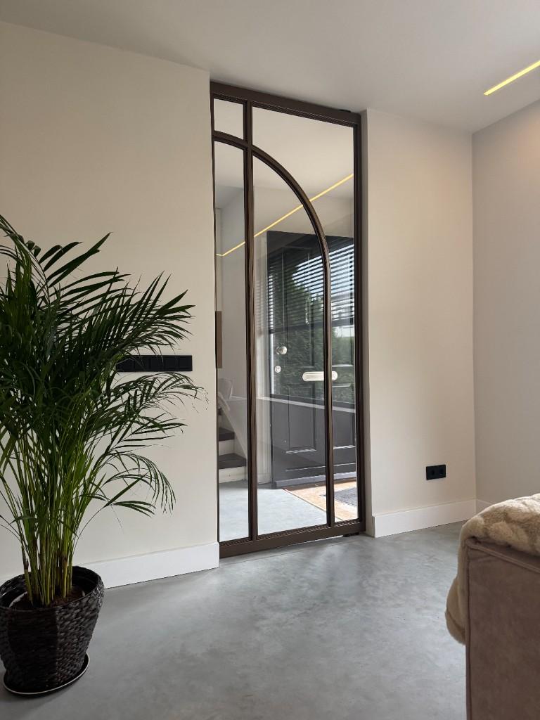 Stalen deur met boog, naast een palm in een lichte kamer